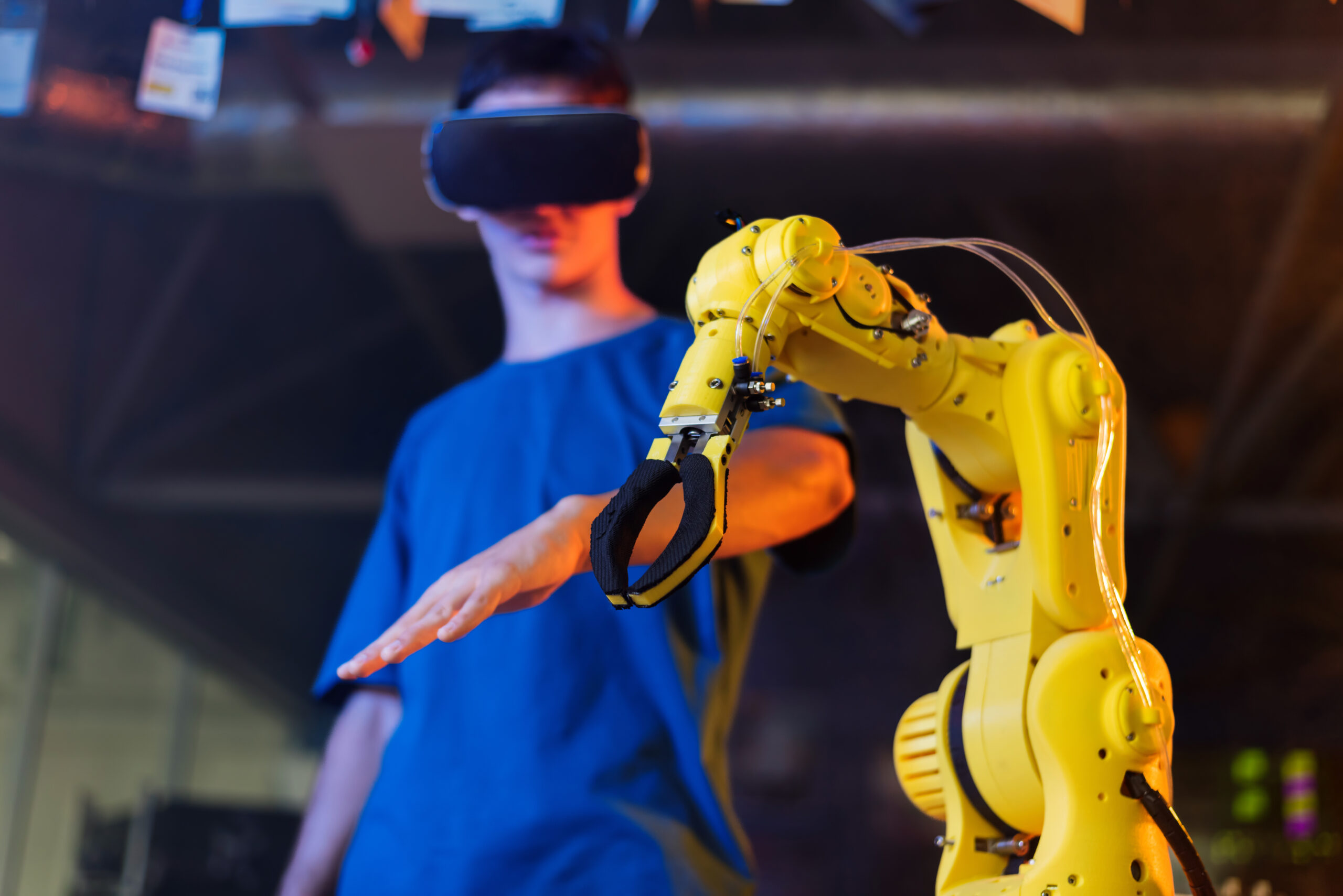 Teen doing experiments in robotics in a laboratory. Boy in VR headset controlling the robot using hand. Red and blue illumination